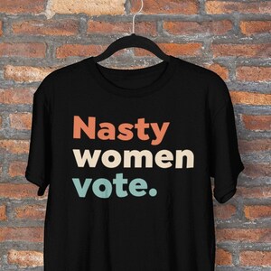 Pu&ograve; includere: Maglietta nera con il testo "Nasty women vote." in caratteri retr&ograve; colorati.