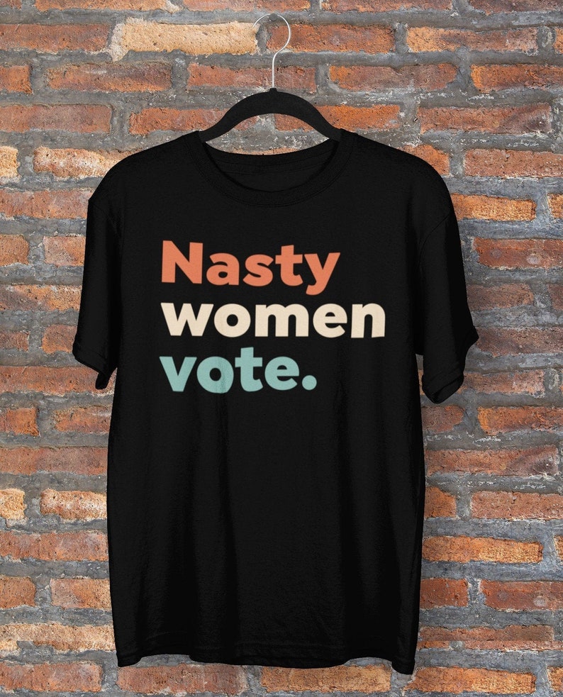 Pu&ograve; includere: Maglietta nera con il testo "Nasty women vote." in caratteri retr&ograve; colorati.
