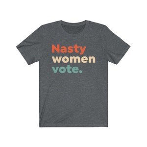 Pu&ograve; includere: Una maglietta grigio scuro melange con il testo "Nasty women vote." in un font retr&ograve; con colori rosso, arancione, giallo e blu.