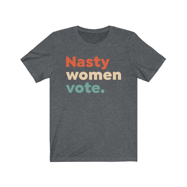 Pu&ograve; includere: Una maglietta grigio scuro melange con il testo "Nasty women vote." in un font retr&ograve; con colori rosso, arancione, giallo e blu.