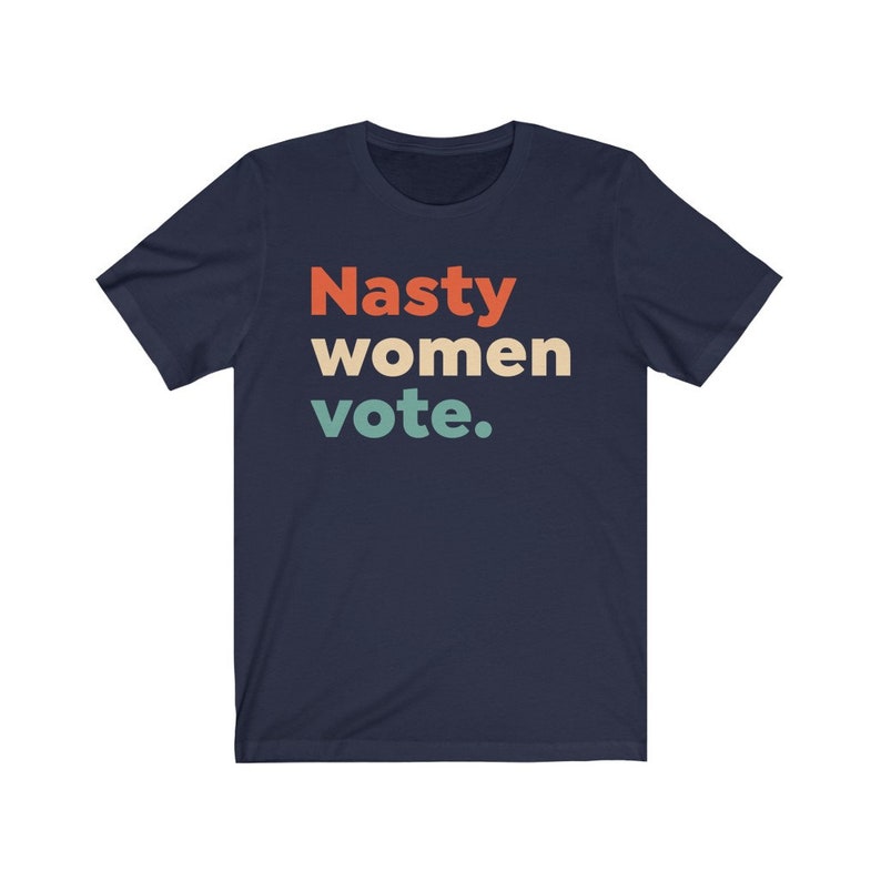Pu&ograve; includere: Una t-shirt blu navy con il testo "Nasty women vote." in un font retr&ograve; con colori arancio, giallo e verde.
