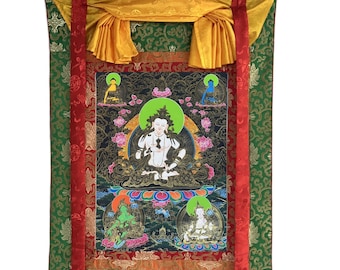 Può includere: Un dipinto thangka tibetano tradizionale che raffigura una divinità seduta con un'aureola verde. Il dipinto è incorniciato da un bordo dorato e circondato da un tessuto colorato con motivi.