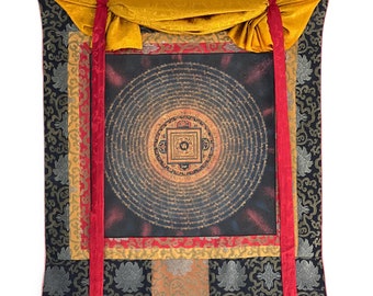 Puede incluir: Un rollo de oración tibetano tradicional con letras doradas y negras sobre un fondo oscuro. El rollo está enmarcado con ribetes rojos y dorados y tiene una cortina de seda amarilla en la parte superior.