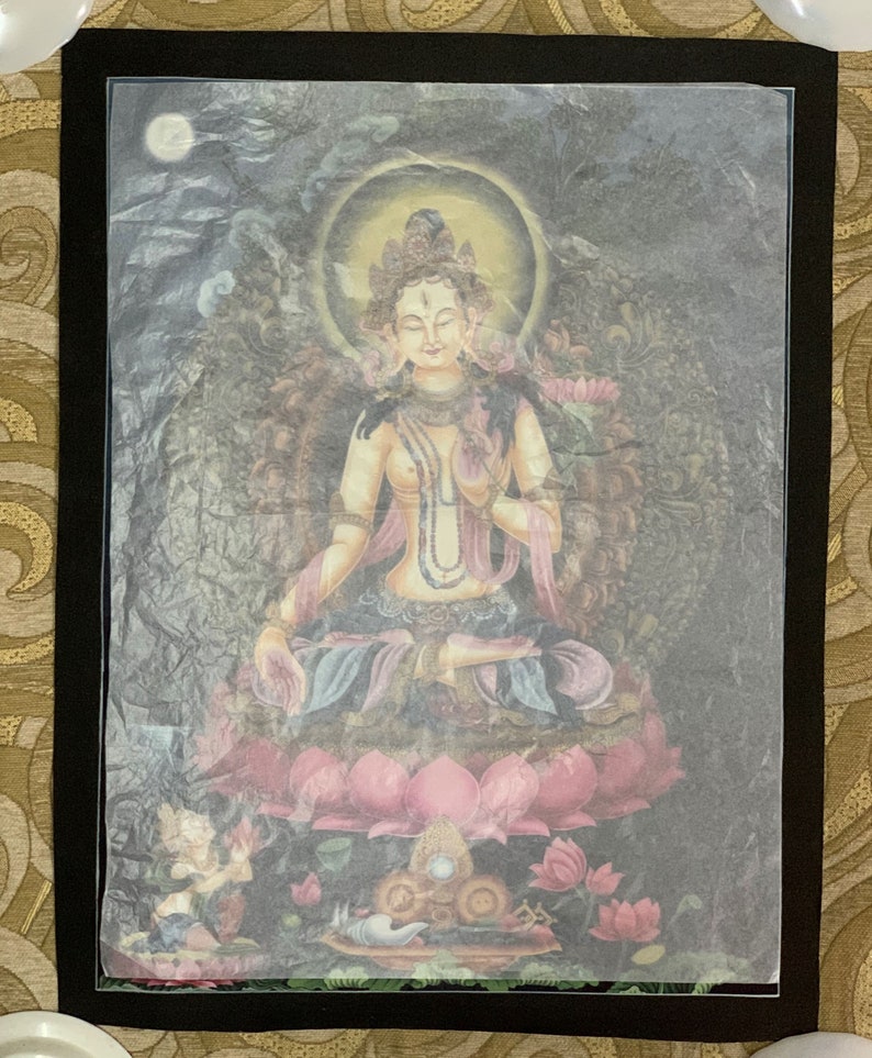May include: A colorful painting of a deity sitting on a lotus flower. The deity is wearing a crown and jewelry and has a serene expression. The painting is framed in black.