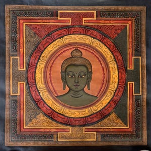 May include: A detailed painting of Buddha's head and shoulders, centered within a circular design. The artwork features a dark green Buddha against a warm orange background, surrounded by ornate red and gold patterns. The square frame has a dark blue background.