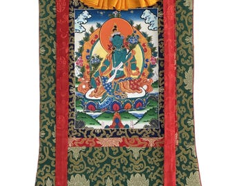 May include: A framed Tibetan thangka painting featuring a seated deity with a blue complexion, surrounded by a golden halo. The artwork is set against a backdrop of clouds and flowers, with a green and gold patterned fabric border and red ribbons.
