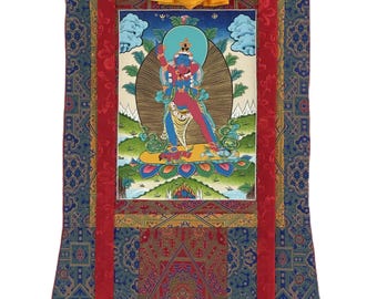 May include: A vertical wall hanging scroll featuring a central painting of a blue deity figure standing on a lotus base. The artwork is framed by red fabric borders and a blue patterned textile mount, topped with a draped yellow silk cloth.