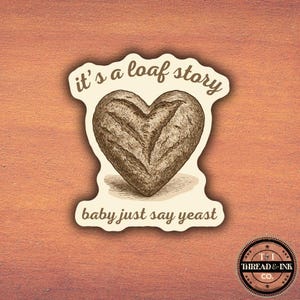 Könnte beinhalten: Ein Aufkleber mit einer herzförmigen Brotillustration. Der Text "it's a loaf story" wölbt sich über dem Brot, und "baby just say yeast" steht darunter. Der Aufkleber hat einen cremefarbenen Rand und befindet sich auf einem orangefarbenen Hintergrund.