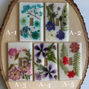 May include: Five white light switch covers with pressed flowers and glitter. The covers are labeled A-1 through A-5.