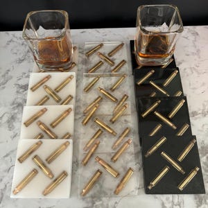 May include: Set of six square drink coasters with a black and white design featuring gold bullet casings. The coasters are arranged in two rows of three.