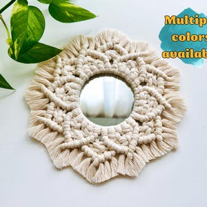 May include: A white macrame mirror with a round mirror in the center. The mirror is surrounded by a decorative macrame design with fringe. Multiple colors available.