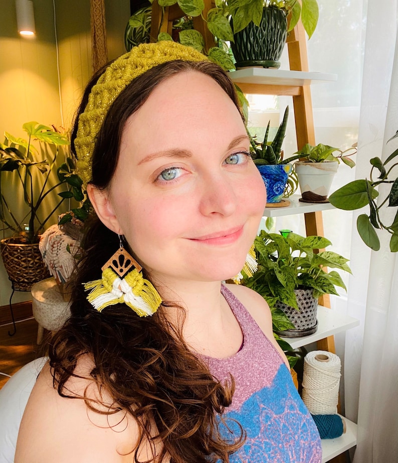 Pu&ograve; includere: Una donna con lunghi capelli castani che indossa una fascia per capelli in crochet gialla e orecchini a nappa gialli e bianchi. Indossa una canotta viola e blu.