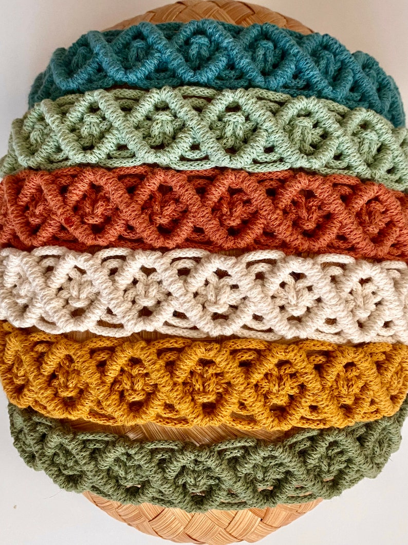 Pu&ograve; includere: Un set di sei fasce per capelli in macram&egrave; di vari colori, tra cui turchese, verde, arancione, crema, giallo senape e verde oliva. Le fasce sono realizzate con un motivo annodato e sono disposte in una pila.
