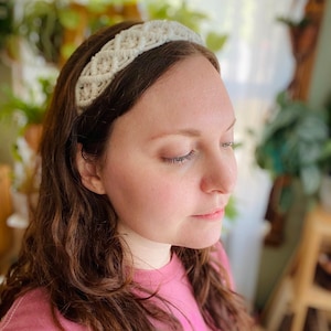 Pu&ograve; includere: Un cerchietto bianco all'uncinetto con un design intrecciato. Il cerchietto &egrave; indossato da una persona con capelli lunghi e castani.