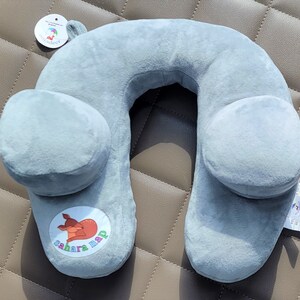 May include: Gray travel neck pillow with a cartoon deer logo that says "sahara nap". The pillow has two side wings for added support.