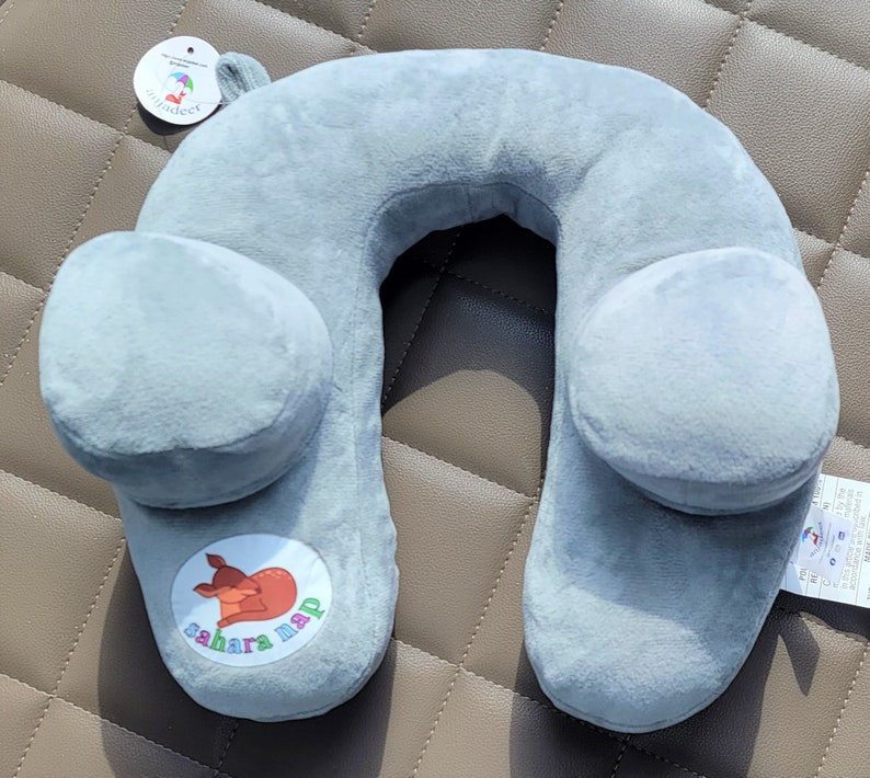 May include: Gray travel neck pillow with a cartoon deer logo that says "sahara nap". The pillow has two side wings for added support.