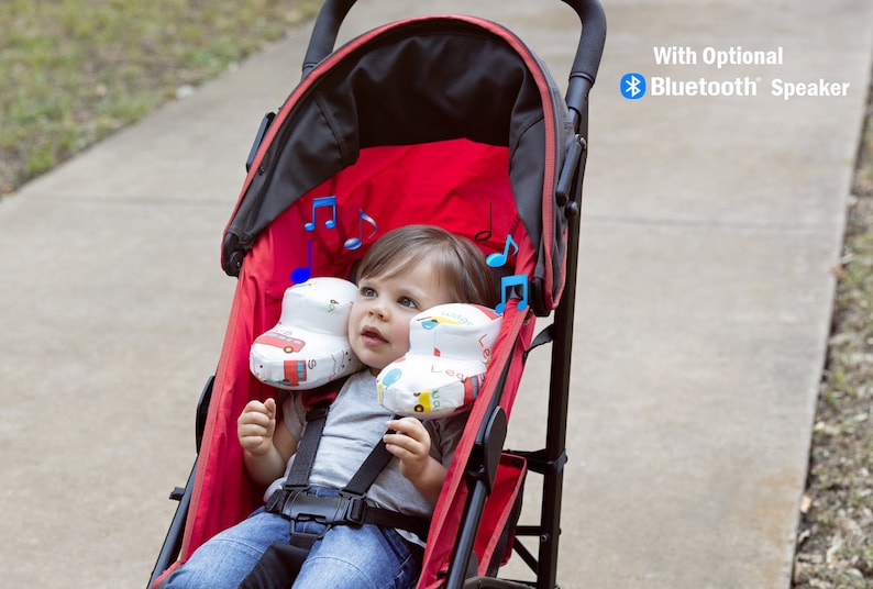May include: A red stroller with a baby sitting inside. The baby is wearing a grey shirt and blue jeans. The stroller has a black canopy and a black handle. The stroller has two white and blue patterned headrests with musical notes printed on them. The stroller has a black basket underneath. The text "With Optional Bluetooth Speaker" is printed in the upper right corner of the image.
