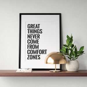 May include: A black framed print with the text "GREAT THINGS NEVER COME FROM COMFORT ZONES" on a white background. A gold lamp and a potted green plant are on a brown shelf.