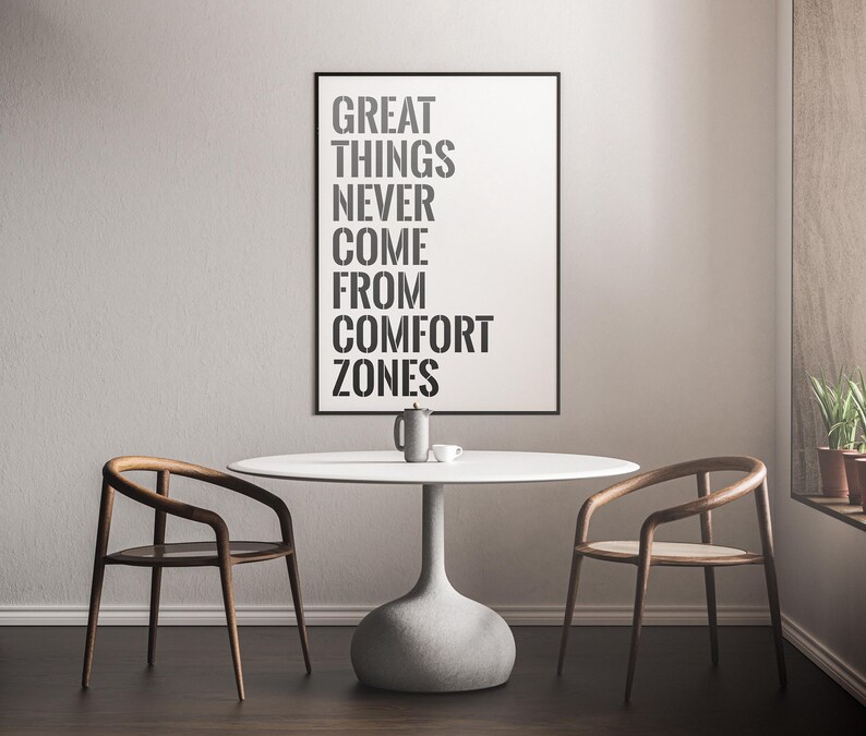 May include: A white table with two wooden chairs and a black framed poster with the text "GREAT THINGS NEVER COME FROM COMFORT ZONES".