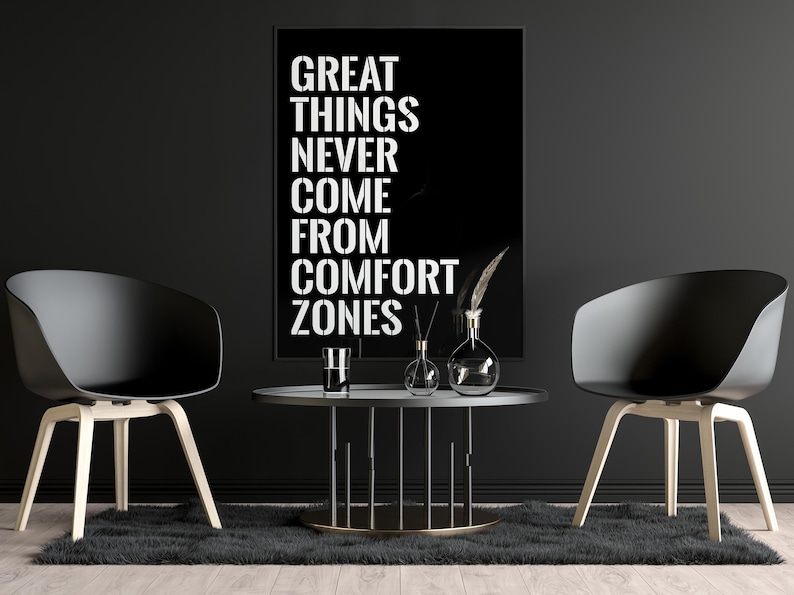 May include: Black and white motivational quote poster with the text "GREAT THINGS NEVER COME FROM COMFORT ZONES" hanging on a black wall with two black chairs and a black coffee table with decorative items.