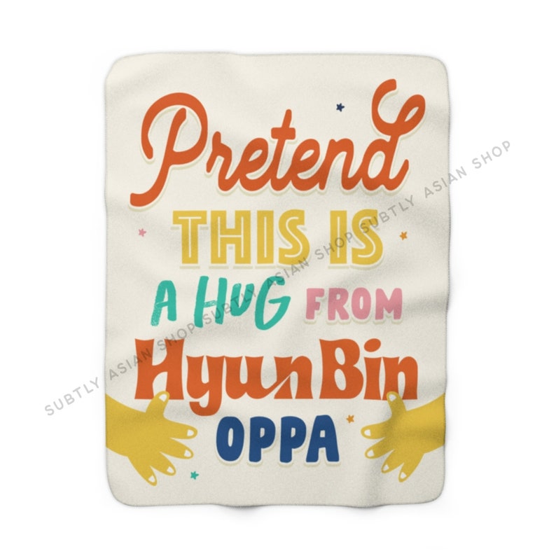 Pu&ograve; includere: Una coperta color crema con il testo "Pretend this is a hug from Hyun Bin Oppa" in lettere colorate e stilizzate. Il testo &egrave; circondato da piccole stelle e due mani gialle che si tendono per un abbraccio.