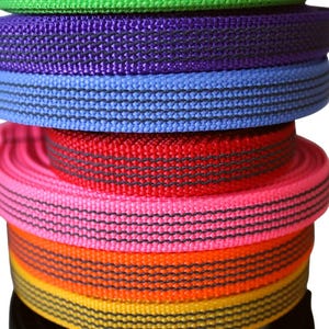 Puede incluir: Una pila de rollos de cincha de nailon de colores. Los rollos son de varios colores, incluyendo verde azulado, verde, morado, azul, rojo, rosa, naranja, amarillo, gris y negro. Cada rollo tiene una franja negra en el centro.