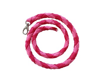 May include: A braided lanyard featuring a repeating pattern of light pink and dark pink woven fabric strands. The cord is coiled into a circular shape and includes a silver-toned metal lobster claw clasp attached to one end for secure fastening.