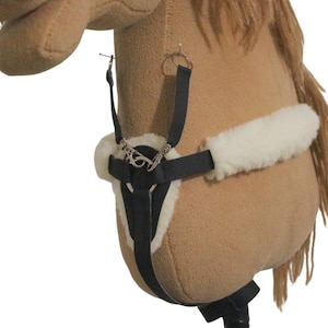 Op de afbeelding: Een bruin stokpaard met een zwart harnas en witte fleece voering. Het paard heeft een bruine manen en staart. Het harnas heeft zilverkleurige metalen hardware. Het paard staat op een witte achtergrond.