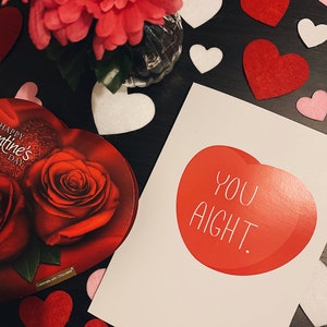 May include: A Valentine's Day card with a red heart and the text "You Aight."  The card is surrounded by red and white felt hearts.
