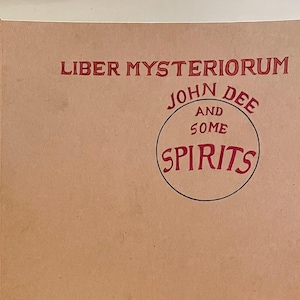 May include: A book cover with the title "Liber Mysteriorum" in red letters. Below, a circular design reads "John Dee and Some Spirits" in red. The cover is a light brown color.