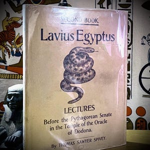 May include: A hardback book titled Lavius Egyptus, Second Book, Lectures Before the Pythagorean Senate in the Temple of the Oracle of Dodona by Thomas Sawyer Spivey. The tan cover features a central black and white illustration of a coiled snake.