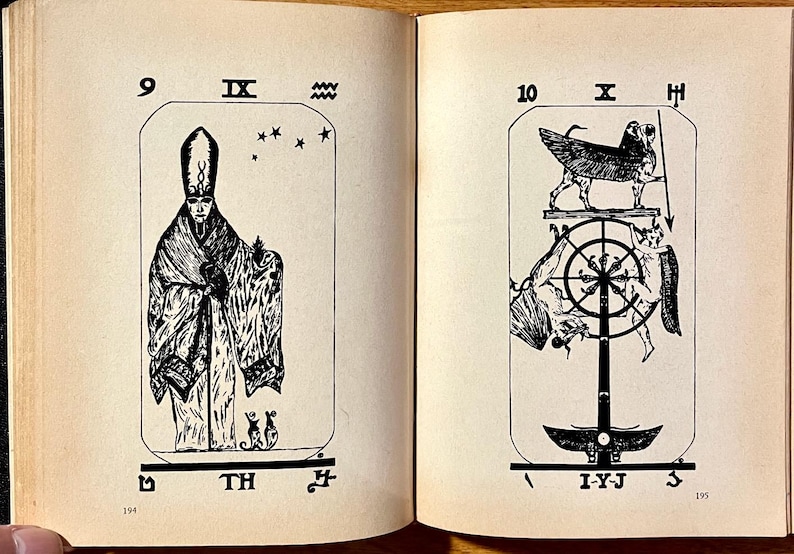 Op de afbeelding: Dubbele pagina uit een oud boek met zwart-wit illustraties van tarotkaarten. De linkerpagina toont een figuur in een gewaad met een hoge hoed, en de rechterpagina toont een gevleugeld wezen boven een wiel.
