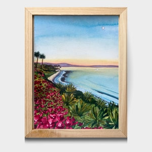 May include: Watercolor painting of a coastal scene with a beach, ocean, and a hillside covered in pink flowers. The sky is blue with a few clouds and a bright sun shining in the distance.