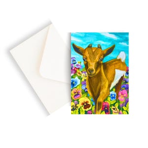 May include: A watercolor greeting card featuring a brown goat standing in a field of colorful pansies. The goat has small horns and a white patch on its side. A white envelope is next to the card.