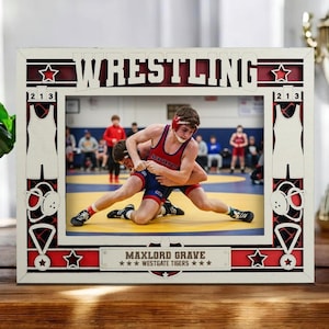 May include: A white and red wooden frame with the word "WRESTLING" at the top. The frame surrounds a photo of two wrestlers in action. The frame also features stars, wrestling singlets, and the text "MAXLORD GRAVE WESTGATE TIGERS".