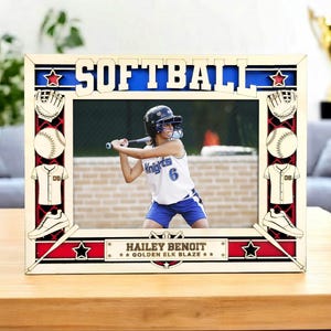 May include: A wooden softball picture frame with the word "SOFTBALL" in blue letters. The frame features softball-themed cutouts, including a glove, ball, jersey, and cleats. The frame holds a photo of a softball player.