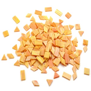 May include: A pile of orange and yellow glass mosaic tiles in various shapes, including squares and triangles. The tiles are scattered on a white background.