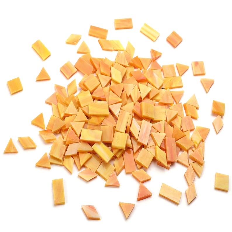 May include: A pile of orange and yellow glass mosaic tiles in various shapes, including squares and triangles. The tiles are scattered on a white background.