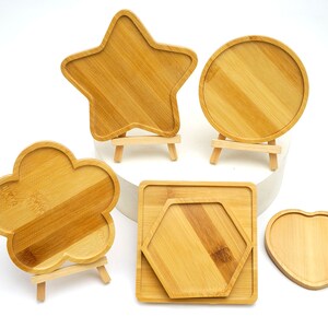 May include: Five wooden trays in different shapes, including a star, a flower, a circle, a hexagon, and a heart. Each tray is on a small wooden stand.