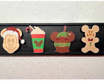 Könnte beinhalten: Vier Weihnachts-Mickey-Mouse-Anhänger. Die Anhänger sind ein Lebkuchenmann, eine Mickey Mouse mit einem Weihnachtsmann-Hut, eine Mickey Mouse mit einer grünen Elfenmütze und eine rot-grüne Mickey-Mouse-Tasse mit Schlagsahne und einem Zuckerstangen.