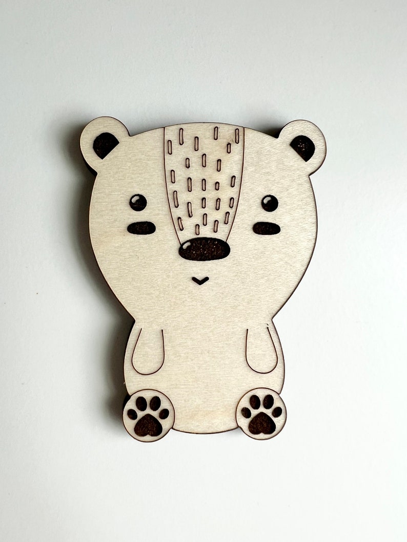 May include: A wooden cutout of a bear with a brown nose and black eyes. The bear has a pattern of small circles on its back and paw prints on its feet.