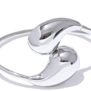 May include: A silver bangle bracelet with two teardrop-shaped charms. The charms are connected to the bangle and are positioned to look like a yin-yang symbol.