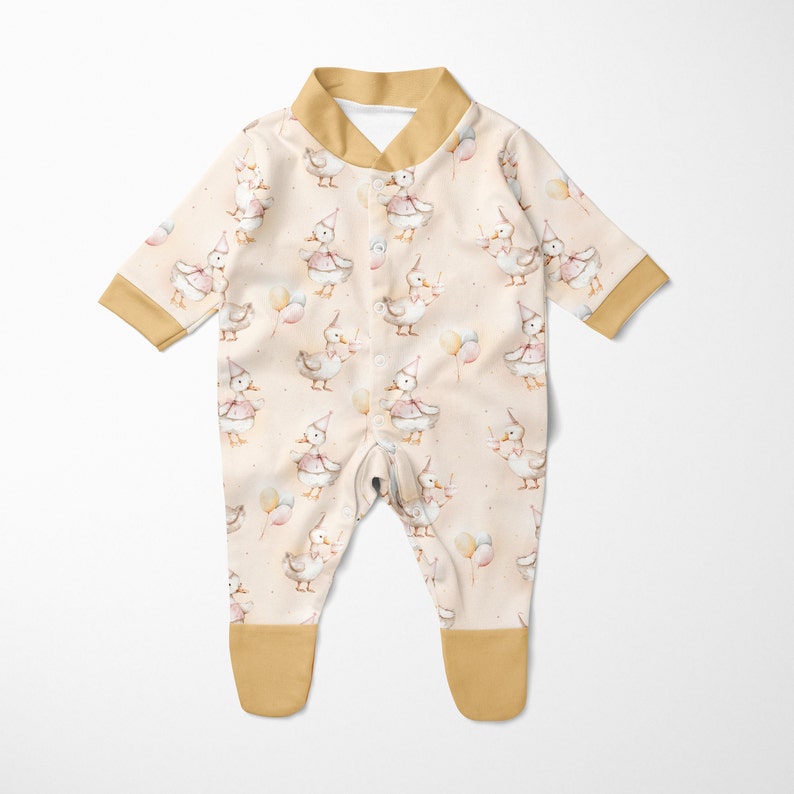 May include: A cream-coloured baby onesie with a mustard yellow collar and cuffs. The onesie features a repeating pattern of watercolour ducks wearing party hats and holding balloons.