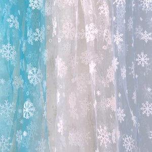 May include: Three sheer fabric panels with snowflake patterns. The panels are light blue, white, and a lighter shade of blue.