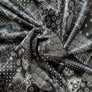May include: Black and white paisley patterned fabric. The fabric features a repeating design of swirling patterns, dots, and floral motifs. The fabric is folded, creating shadows and highlights that emphasize the texture and design.