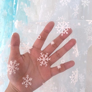 May include: White sheer fabric with snowflake embroidery. The fabric is translucent and has a delicate, airy feel.