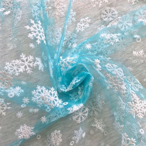 May include: Light blue tulle fabric with white snowflake embroidery. The fabric is gathered and twisted, showing the texture of the tulle.