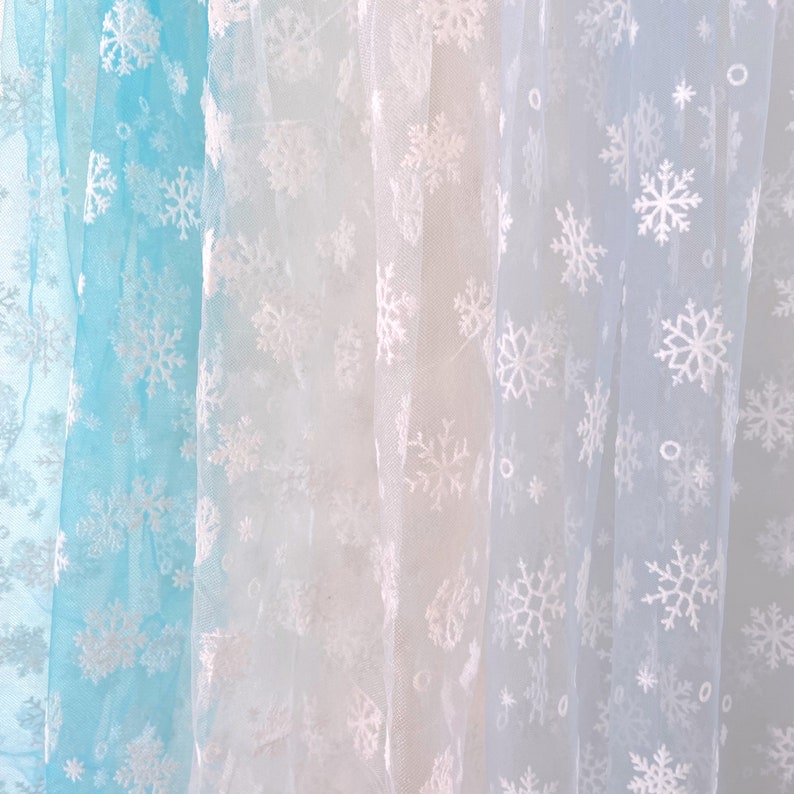 May include: Three sheer fabric panels with a snowflake pattern. The panels are in shades of blue, white, and light blue.