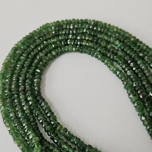 May include: A strand of small, faceted, forest green gemstone beads arranged in a curved formation. Each individual bead features a polished, multi-faceted surface that reflects light, creating a consistent, deep green color throughout the entire strand.