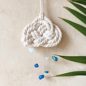 May include: A white macrame cloud with blue and green gemstone raindrops hanging from it.